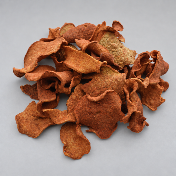 Chips de jícama deshidratada con adobo, de formas irregulares, agrupados sobre fondo gris claro.