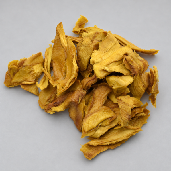 Piezas de mango deshidratado natural, de tonos amarillos y anaranjados, sobre fondo gris claro.